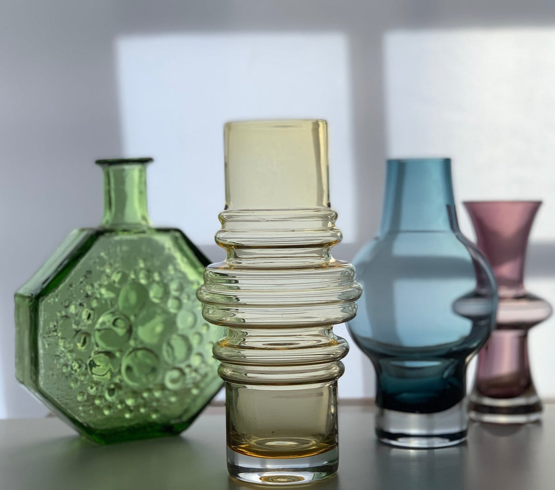 Green, amber, blue and pink Scandinavian modern glass vases arranged in window light.