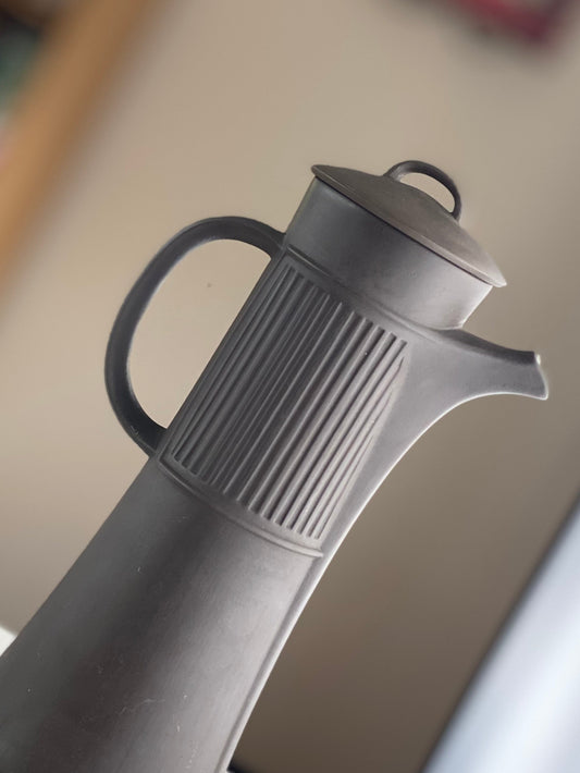 Close-up of a dark ceramic teapot showing its curved handle, lid and sculpted spout.
