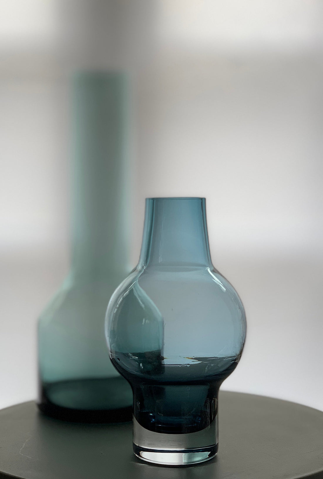 Blue glass vase in focus with a second vase by the same designer softly blurred in the background.