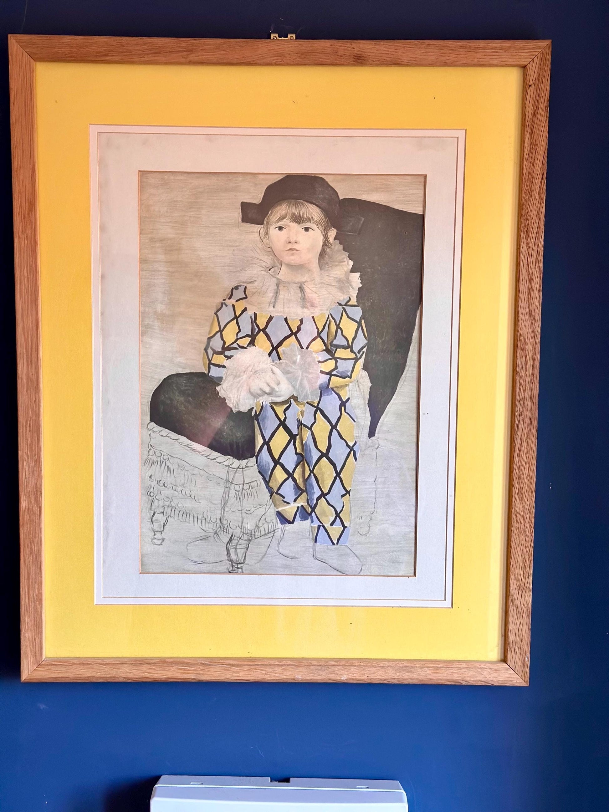 Full-frame view of a vintage Pablo Picasso print titled "The Artist's Son" (Paul en Pierrot) in a minimalist light oak gallery frame with a wide double yellow/off-white mount.
